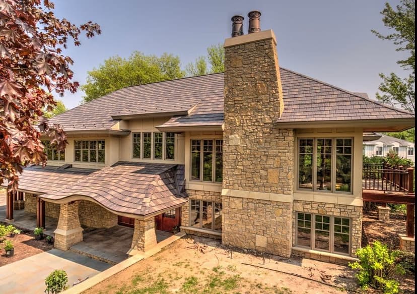 Modern stone house with a unique roof design and large windows surrounded by greenery.