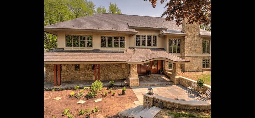 Modern stone house with large windows and landscaped garden, surrounded by trees.